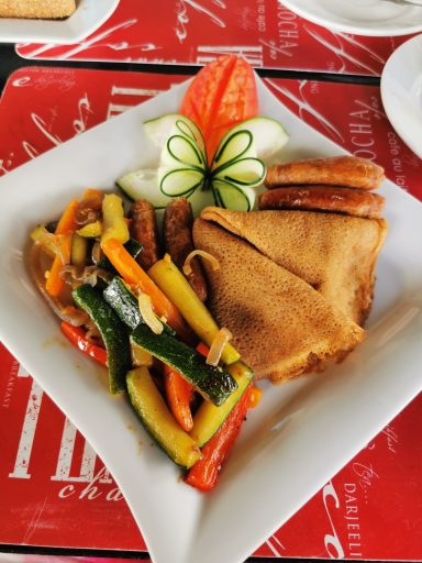 Buntes Gemüsegericht mit Crêpe und dekorativem Obst.